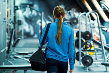 Fit woman in sportswear entering gym, blurred equipment. Young female preparing for training....