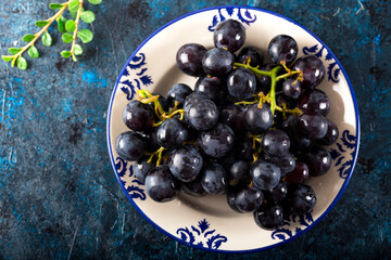 Bunch of grape with water drops in ceramic dish on dark background. Fresh black grapes.