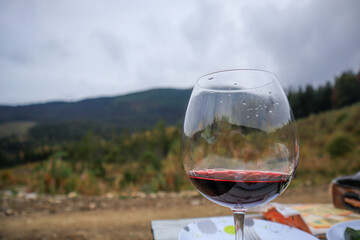 Photo of wine pouring out of a glass on a background of mountains. Female hand. Ukrainian Carpathian Mountains