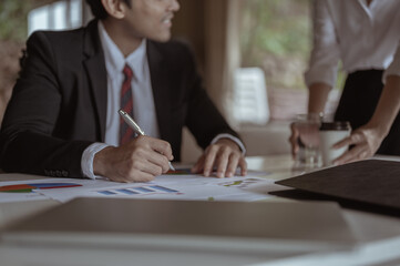 A businessman decides to sign a business contract..The secretary is serving water and coffee.