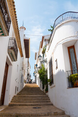 Beautiful narrow street in Altea, Costa Blanca, Valencian Community, Spain. Historical center/old town. Stone stairs going up with no tourist. Vertical shot. Typical ancient architecture.