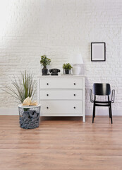 Decorative white cabinet and black chair in front of the brick wall, lamp, frame and vase of plant decorative style.