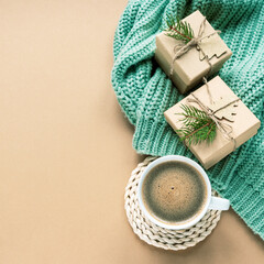 A cup of coffee and Christmas gifts on green sweater on beige background, top view, copy space
