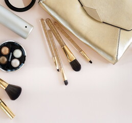 Womens makeup decorative cosmetics, accessories and golden bag on pink background top view.Copy space. Fashion background.