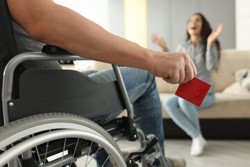 Man in wheelchair holds condom in hand close-up in front of joyful girl. Disability sexuality and...