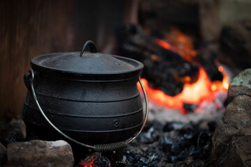 Cast iron pot cooking over red hot coles - obrazy, fototapety, plakaty