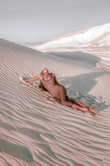 young woman in black mesh dress is laying fashion on the sand in desert at sunset, fashion concept, free space