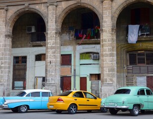 Fototapeta na wymiar Multicolored vintage cars in front of an old colonial house facade in Havana, Cuba