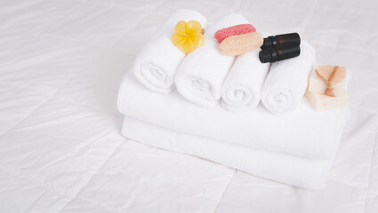 Spa object with  white towels,organic soap,luffa scrub, and plumerai flower candle on clean white bedding.