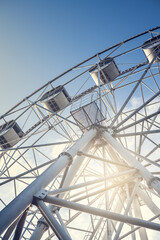 Gray or white metal ferris wheel with closed passenger cabins close-up in the amusement park