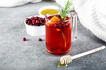 tea with cranberries, cinnamon , orange, rosemary and honey in a glass cup on a gray background, white sweater