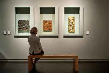 rear view of woman sitting in an art gallery in front of colorful paintings