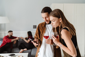 Image of multinational friends using mobile phone while drinking wine