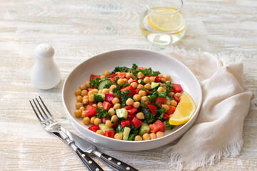 Healthy vegan salad with chickpeas, tomatoes, cucumbers, bell peppers and kale on light wooden...