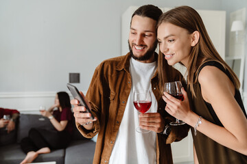 Image of multinational friends using mobile phone while drinking wine