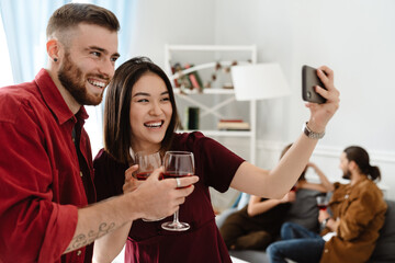 Image of joyful friends taking selfie on cellphone while drinking wine