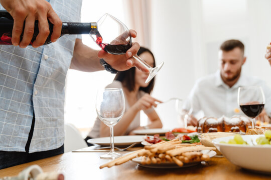 Image of happy young friends drinking wine while having lunch