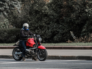 A motorcycle rider in a closed helmet sits on an unknown red sports bike during the day. The motorcyclist stopped on the asphalt with dense plants in the background. Freedom concept.