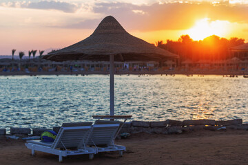 Empty sunbeds and natural umbrellas at beach with setting sun
