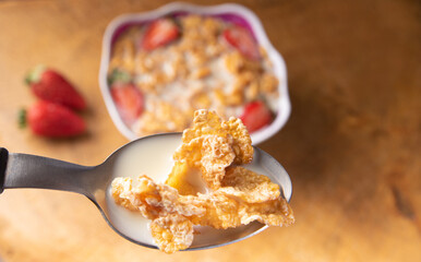Breakfast cereal, corn flakes, strawberries and milk, in the foreground a spoon with corn flakes and milk. selective focus.