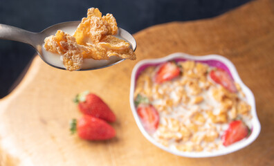 Breakfast cereal, corn flakes, strawberries and milk, in the foreground a spoon with corn flakes and milk. selective focus.