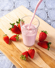 Putting strawberry juice in a glass on wood with strawberries around it, Top view.