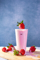 Strawberry making a splash on Strawberry juice in a glass on wood with strawberries around, blue gradient background, selective focus.