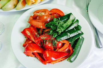 Slice of cucumbers, tomatoes, peppers on a white plate on the background of the table. Close up
