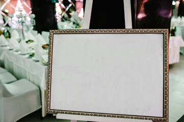 List, plan, chart of the seating area of guests at the tables at restaurant. Tables wedding guests on the easel on wedding reception. The frame is decorated. Frame. Place for text.