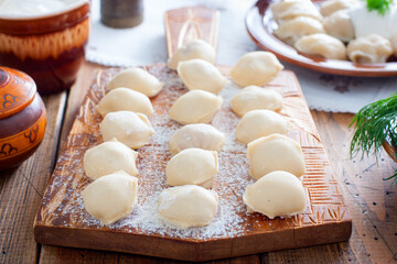 Fototapeta na wymiar Raw homemade dumplings on a wooden board, selective focus