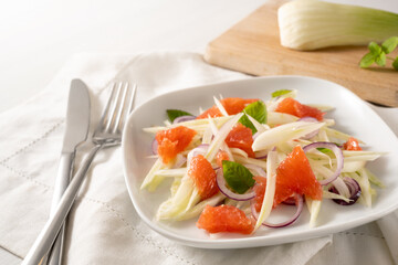 Fresh salad from raw fennel slices, grapefruit and red onions on a white plate, healthy vegetarian food, selected focus