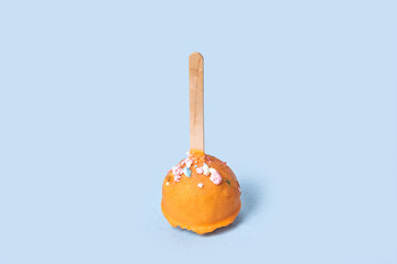 Chocolate dessert in orange glaze. Round pastry on a wooden stick. Blue background.
