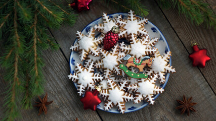 plate with ginger cookies in the form of snowflakes with lying next to red Christmas decorations and fir branches on a wooden background close-up. Merry Christmas and Happy New Year holiday.