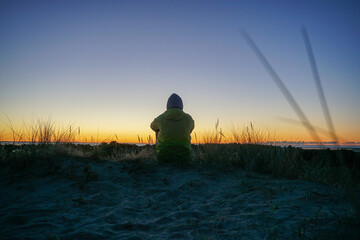 Junger Mann blickt alleine in den Sonnenaufgang in den Dünen