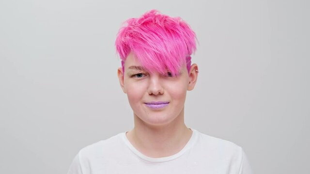 Young beautiful girl with a short haircut and pink hair. A homosexual lesbian model poses on a white background in the studio.