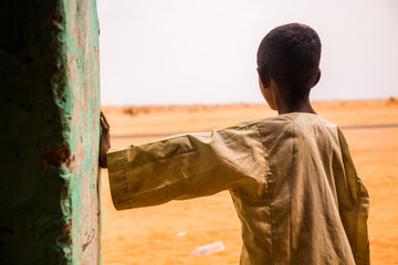 Sudanese boy looking into the desert leaning to a wall