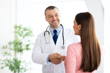 Obraz premium Portrait of middle aged doctor handshaking with his patient