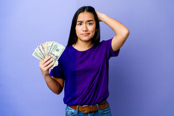 Young asian woman holding money isolated on purple background being shocked, she has remembered important meeting.