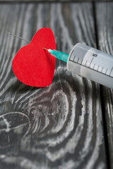 A paper heart pierced with a medical syringe. Against the background of pine boards in black.