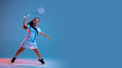 Fototapeta na wymiar Motion. Beautiful dwarf woman practicing in badminton isolated on blue background in neon light. Lifestyle of inclusive people, diversity and equility. Sport, activity and movement. Copyspace, flyer