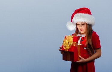 a surprised baby girl in a red Santa hat holds a Christmas gift in her hand.