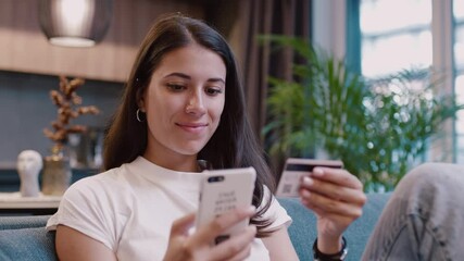 Smiling woman use phone and credit card number for online shopping sitting at home. Smartphone communication technology banking money. Slow motion