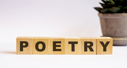 The word POETRY on wooden cubes on a light background near a flower in a pot. Defocus
