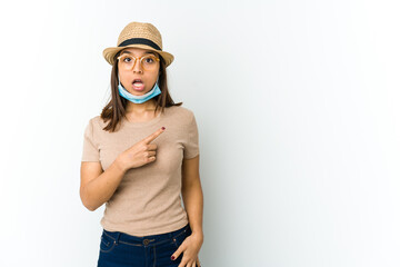 Young latin woman wearing hat and mask to protect from covid isolated on white background pointing to the side