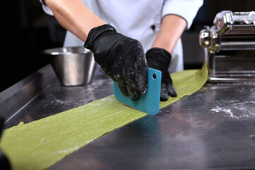 The chef cuts the prepared pasta dough into portions. Homemade dough with spinach. Unrecognizable person. Hands in protective black gloves.Machine for preparing pasta or a pasta machine.