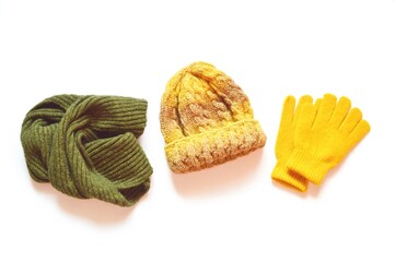 Green woolen scarf, yellow knitted hat and gloves isolated on a white background. Flat lay autumn and winter clothes. Bright accessories for stylish outfit