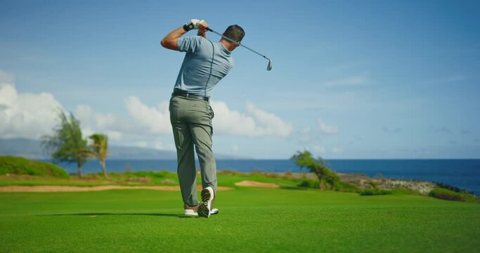 Golfer swinging and hitting golf ball on beautiful course by the ocean, slow motion, resort travel vacation concept