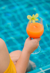 Woman dink a cocktail glass of orange juice at swimming pool. Summer holiday and relax alone at...