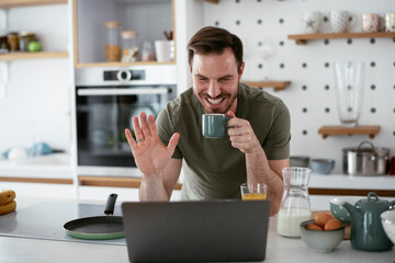 Handsome man drinking coffee in kitchen. Young man having video call.