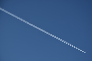 A single plane flies across the blue sky. Jet traili on blue sky.